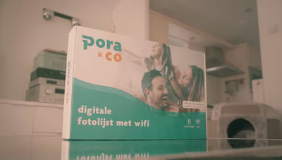 Pora & Co digitale fotolijst met Wi-Fi, getoond in de verpakking op een glazen tafel in een huiselijke omgeving.